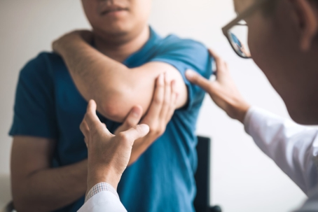 A dirt path running through a corn maze between tall stalks of green and golden corn, with a wooded hill of fall foliage and a bright blue sky in the background.